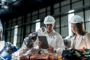 Factory engineers inspecting on machine with smart tablet. Worker works at machine robot arm. The welding machine with a remote system in an industrial factory. Artificial intelligence concept. photo