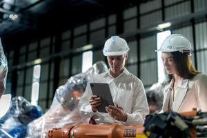 Factory engineers inspecting on machine with smart tablet. Worker works at machine robot arm. The welding machine with a remote system in an industrial factory. Artificial intelligence concept. photo