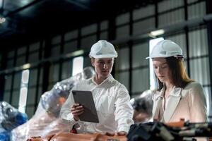Factory engineers inspecting on machine with smart tablet. Worker works at machine robot arm. The welding machine with a remote system in an industrial factory. Artificial intelligence concept. photo