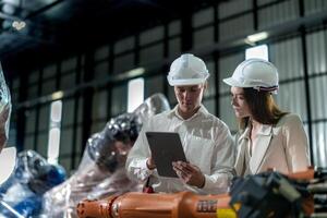 Factory engineers inspecting on machine with smart tablet. Worker works at machine robot arm. The welding machine with a remote system in an industrial factory. Artificial intelligence concept. photo