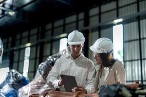 Factory engineers inspecting on machine with smart tablet. Worker works at machine robot arm. The welding machine with a remote system in an industrial factory. Artificial intelligence concept. photo