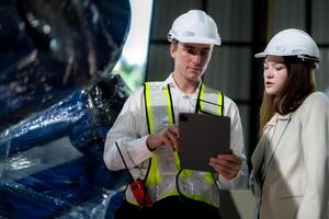 Factory engineers inspecting on machine with smart tablet. Worker works at machine robot arm. The welding machine with a remote system in an industrial factory. Artificial intelligence concept. photo