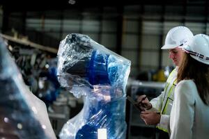 negocio ingenieros reunirse y cheque controlar pesado máquina robot brazo. diverso equipo de industrial robótica ingenieros reunido alrededor máquina. profesional maquinaria operador utilizar industrial digital tableta. foto