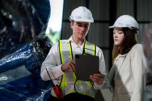 Factory engineers inspecting on machine with smart tablet. Worker works at machine robot arm. The welding machine with a remote system in an industrial factory. Artificial intelligence concept. photo