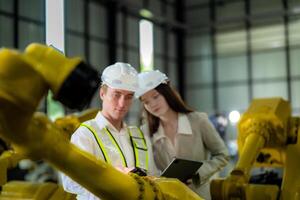 Sales manager and factory owner in suits negotiating selling robots used in the factory. Business engineers meeting and checking new machine robot. Workers walking at warehouse welding machine. photo