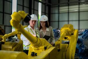 Factory engineers inspecting on machine with smart tablet. Worker works at machine robot arm. The welding machine with a remote system in an industrial factory. Artificial intelligence concept. photo