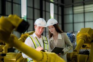 Sales manager and factory owner in suits negotiating selling robots used in the factory. Business engineers meeting and checking new machine robot. Workers walking at warehouse welding machine. photo