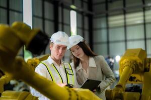 Sales manager and factory owner in suits negotiating selling robots used in the factory. Business engineers meeting and checking new machine robot. Workers walking at warehouse welding machine. photo