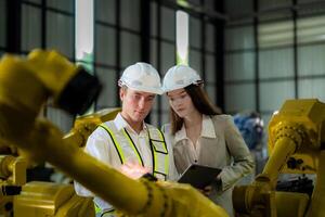 Sales manager and factory owner in suits negotiating selling robots used in the factory. Business engineers meeting and checking new machine robot. Workers walking at warehouse welding machine. photo