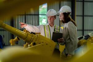 Factory engineers inspecting on machine with smart tablet. Worker works at machine robot arm. The welding machine with a remote system in an industrial factory. Artificial intelligence concept. photo