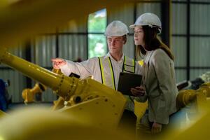 Factory engineers inspecting on machine with smart tablet. Worker works at machine robot arm. The welding machine with a remote system in an industrial factory. Artificial intelligence concept. photo