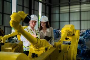 Factory engineers inspecting on machine with smart tablet. Worker works at machine robot arm. The welding machine with a remote system in an industrial factory. Artificial intelligence concept. photo