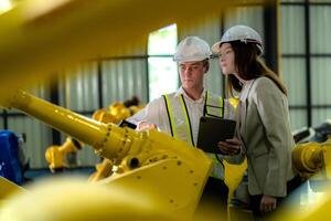 Factory engineers inspecting on machine with smart tablet. Worker works at machine robot arm. The welding machine with a remote system in an industrial factory. Artificial intelligence concept. photo