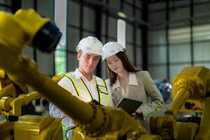 Factory engineers inspecting on machine with smart tablet. Worker works at machine robot arm. The welding machine with a remote system in an industrial factory. Artificial intelligence concept. photo