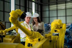 Factory engineers inspecting on machine with smart tablet. Worker works at machine robot arm. The welding machine with a remote system in an industrial factory. Artificial intelligence concept. photo