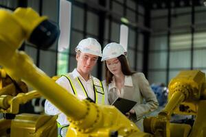 Factory engineers inspecting on machine with smart tablet. Worker works at machine robot arm. The welding machine with a remote system in an industrial factory. Artificial intelligence concept. photo
