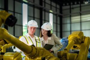 Factory engineers inspecting on machine with smart tablet. Worker works at machine robot arm. The welding machine with a remote system in an industrial factory. Artificial intelligence concept. photo