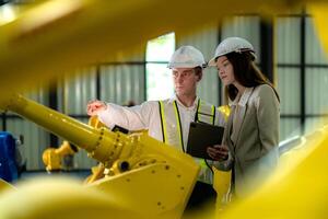 Factory engineers inspecting on machine with smart tablet. Worker works at machine robot arm. The welding machine with a remote system in an industrial factory. Artificial intelligence concept. photo