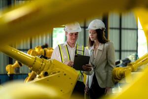 Factory engineers inspecting on machine with smart tablet. Worker works at machine robot arm. The welding machine with a remote system in an industrial factory. Artificial intelligence concept. photo