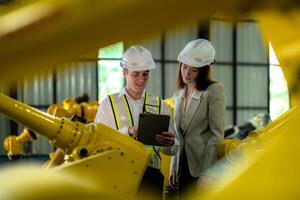 Factory engineers inspecting on machine with smart tablet. Worker works at machine robot arm. The welding machine with a remote system in an industrial factory. Artificial intelligence concept. photo