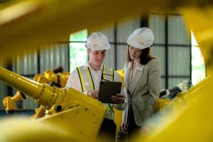 Factory engineers inspecting on machine with smart tablet. Worker works at machine robot arm. The welding machine with a remote system in an industrial factory. Artificial intelligence concept. photo