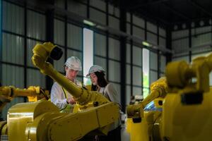 Factory engineers inspecting on machine with smart tablet. Worker works at heavy machine robot arm. The welding machine with a remote system in an industrial factory. Artificial intelligence concept. photo