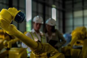 Factory engineers inspecting on machine with smart tablet. Worker works at heavy machine robot arm. The welding machine with a remote system in an industrial factory. Artificial intelligence concept. photo