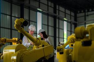 Factory engineers inspecting on machine with smart tablet. Worker works at heavy machine robot arm. The welding machine with a remote system in an industrial factory. Artificial intelligence concept. photo