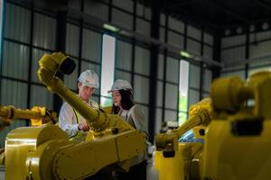 Factory engineers inspecting on machine with smart tablet. Worker works at heavy machine robot arm. The welding machine with a remote system in an industrial factory. Artificial intelligence concept. photo