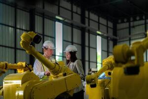 Factory engineers inspecting on machine with smart tablet. Worker works at heavy machine robot arm. The welding machine with a remote system in an industrial factory. Artificial intelligence concept. photo