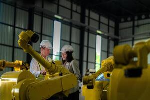 Factory engineers inspecting on machine with smart tablet. Worker works at heavy machine robot arm. The welding machine with a remote system in an industrial factory. Artificial intelligence concept. photo