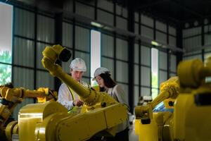 Factory engineers inspecting on machine with smart tablet. Worker works at heavy machine robot arm. The welding machine with a remote system in an industrial factory. Artificial intelligence concept. photo