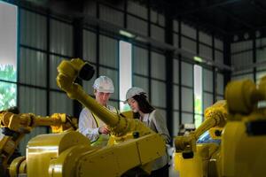 Factory engineers inspecting on machine with smart tablet. Worker works at heavy machine robot arm. The welding machine with a remote system in an industrial factory. Artificial intelligence concept. photo