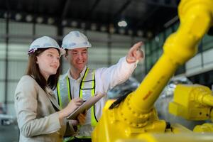 fábrica ingenieros inspeccionando en máquina con inteligente tableta. trabajador trabajos a pesado máquina robot brazo. el soldadura máquina con un remoto sistema en un industrial fábrica. artificial inteligencia concepto. foto