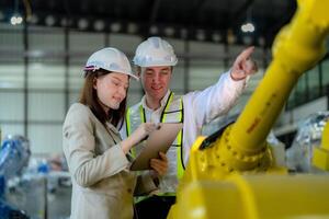 fábrica ingenieros inspeccionando en máquina con inteligente tableta. trabajador trabajos a pesado máquina robot brazo. el soldadura máquina con un remoto sistema en un industrial fábrica. artificial inteligencia concepto. foto