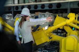 fábrica ingenieros inspeccionando en máquina con inteligente tableta. trabajador trabajos a pesado máquina robot brazo. el soldadura máquina con un remoto sistema en un industrial fábrica. artificial inteligencia concepto. foto