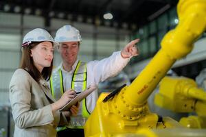 Factory engineers inspecting on machine with smart tablet. Worker works at heavy machine robot arm. The welding machine with a remote system in an industrial factory. Artificial intelligence concept. photo