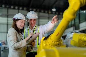 Factory engineers inspecting on machine with smart tablet. Worker works at heavy machine robot arm. The welding machine with a remote system in an industrial factory. Artificial intelligence concept. photo