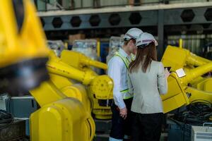 Factory engineers inspecting on machine with smart tablet. Worker works at heavy machine robot arm. The welding machine with a remote system in an industrial factory. Artificial intelligence concept. photo