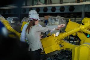 Factory engineers inspecting on machine with smart tablet. Worker works at heavy machine robot arm. The welding machine with a remote system in an industrial factory. Artificial intelligence concept. photo