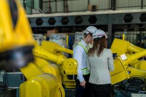 Factory engineers inspecting on machine with smart tablet. Worker works at heavy machine robot arm. The welding machine with a remote system in an industrial factory. Artificial intelligence concept. photo