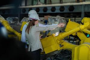 fábrica ingenieros inspeccionando en máquina con inteligente tableta. trabajador trabajos a pesado máquina robot brazo. el soldadura máquina con un remoto sistema en un industrial fábrica. artificial inteligencia concepto. foto