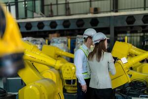 Factory engineers inspecting on machine with smart tablet. Worker works at heavy machine robot arm. The welding machine with a remote system in an industrial factory. Artificial intelligence concept. photo