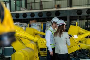 Factory engineers inspecting on machine with smart tablet. Worker works at heavy machine robot arm. The welding machine with a remote system in an industrial factory. Artificial intelligence concept. photo