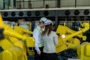 Factory engineers inspecting on machine with smart tablet. Worker works at heavy machine robot arm. The welding machine with a remote system in an industrial factory. Artificial intelligence concept. photo