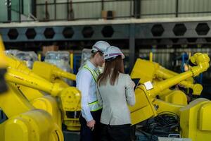 Factory engineers inspecting on machine with smart tablet. Worker works at heavy machine robot arm. The welding machine with a remote system in an industrial factory. Artificial intelligence concept. photo