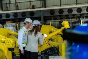 Factory engineers inspecting on machine with smart tablet. Worker works at heavy machine robot arm. The welding machine with a remote system in an industrial factory. Artificial intelligence concept. photo