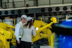 Factory engineers inspecting on machine with smart tablet. Worker works at heavy machine robot arm. The welding machine with a remote system in an industrial factory. Artificial intelligence concept. photo