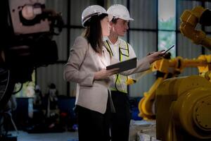 Business woman and man meeting and checking new machine robot. Engineer walking at warehouse industry machine. business negotiation concepts and technology. woman is Using smart Tablet to present man. photo