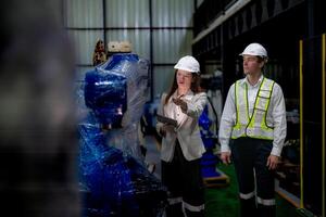 Business woman and man meeting and checking new machine robot. Engineer walking at warehouse industry machine. business negotiation concepts and technology. woman is Using smart Tablet to present man. photo